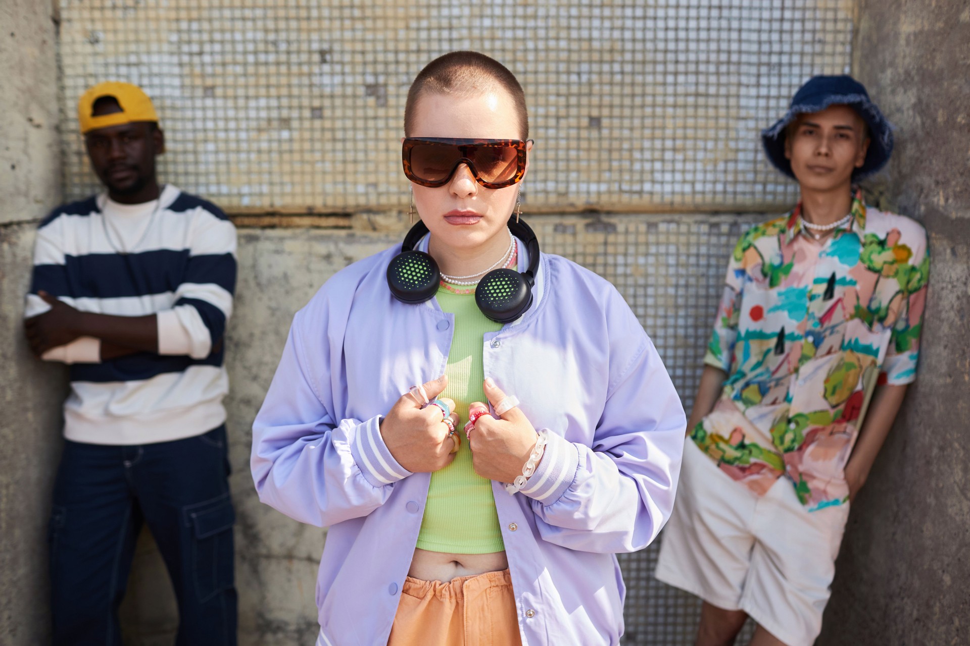 Three young people standing urban with bald young woman in foreground.